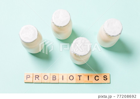 Small bottles with probiotics and prebiotics dairy drink on blue background. Production with biologically active additives. Fermentation and diet healthy food. Bio yogurt with useful microorganisms. 77208692