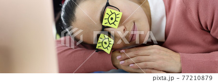Tired woman lies at workplace with stickers on her eyes Tired woman lies at workplace with stickers on her eyes 77210879