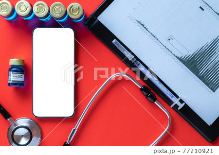 Medical screen. Hospital equipment: doctor stethoscope, hospital healthcare charts, syringe with needle and black smartphone with blank screen on red background. Mockup generic device. 77210921