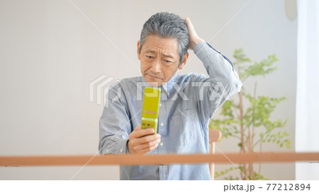携帯電話の操作に悪戦苦闘するシニア男性 77212894