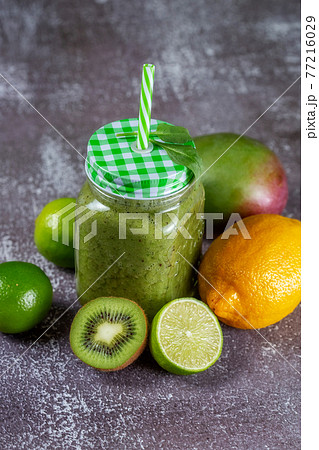 Healthy fresh fruit smoothie drink surrounded by kiwi lime and lemon on gray Healthy fresh fruit smoothie drink surrounded by kiwi lime and lemon on gray 77216029