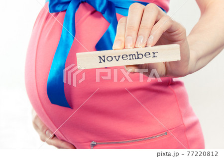 Woman in pregnant wearing pink dress with blue ribbon and showing word november Woman in pregnant wearing pink dress with blue ribbon and showing word november 77220812