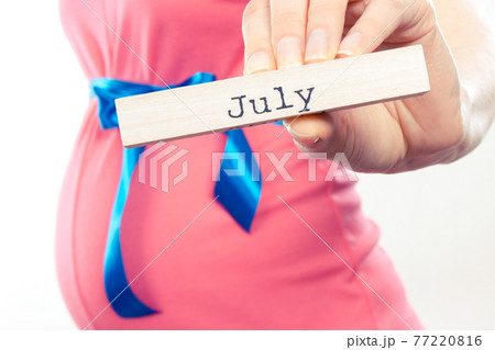 Pregnant woman in pink dress with blue ribbon showing word july Pregnant woman in pink dress with blue ribbon showing word july 77220816