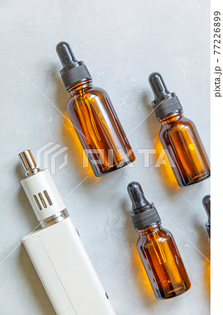Vaping device e-cigarette electronic cigarette and liquid bottles on concrete stone grey background. Vape device for alternative smoking. Vaping shop concept. Gadget for vaper. Vaping accessories. 77226899