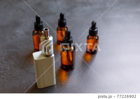 Vaping device e-cigarette electronic cigarette and liquid bottles on dark black stone shale background. Vape device for alternative smoking. Vaping shop concept. Gadget for vaper. Vaping accessories. 77226902