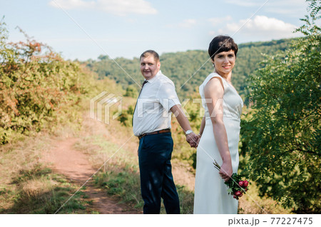 Newlyweds hold hands on the background of the forest 77227475