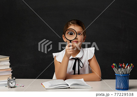 cute little schoolgirl looking through magnifying glass 77229538