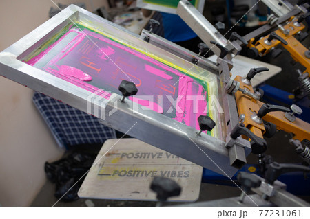 Serigraphy silk screen print process at clothes factory. Frame, squeegee and plastisol color paints 77231061