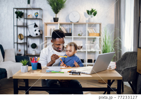 Afro american man working on laptop and playing with son Afro american man working on laptop and playing with son 77233127