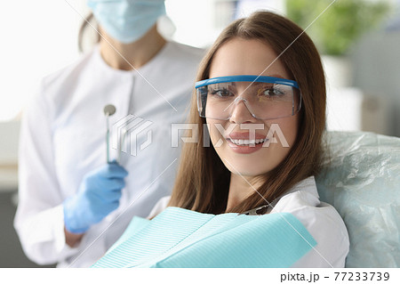 Woman patient in safety glasses sitting in dental chair near doctor Woman patient in safety glasses sitting in dental chair near doctor 77233739