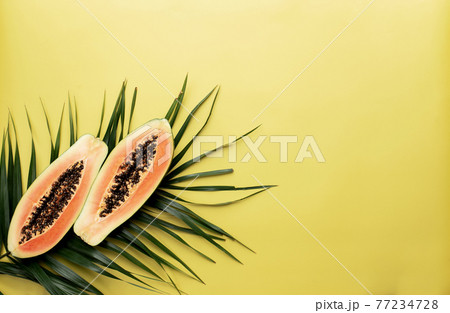 Fresh tropical papaya fruit halves on the palm leaf on a yellow background 77234728