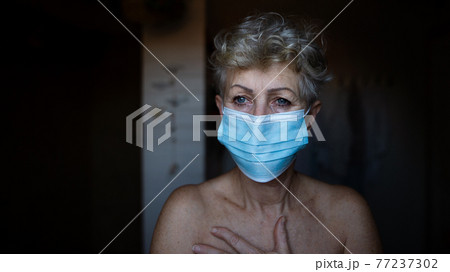 Depressed senior woman with face mask at home, coronavirus and mental health concept. 77237302