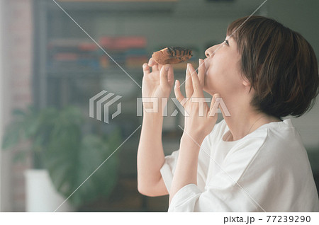 リビングでドーナツを食べる若い女性 77239290