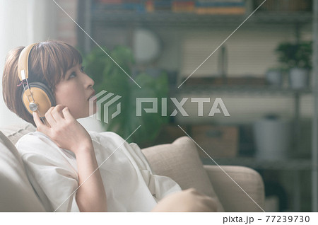 ソファーに座ってヘッドフォンで音楽を聴く若い女性 77239730
