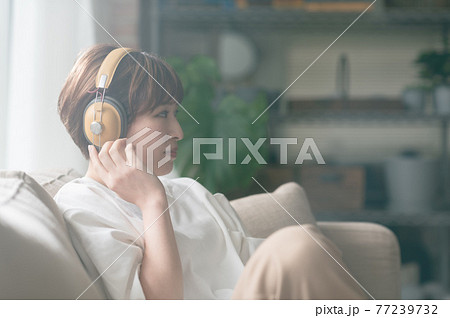 ソファーに座ってヘッドフォンで音楽を聴く若い女性 77239732