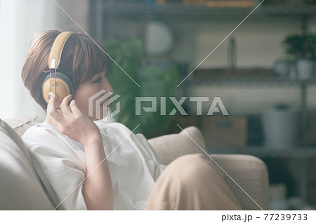 ソファーに座ってヘッドフォンで音楽を聴く若い女性 77239733