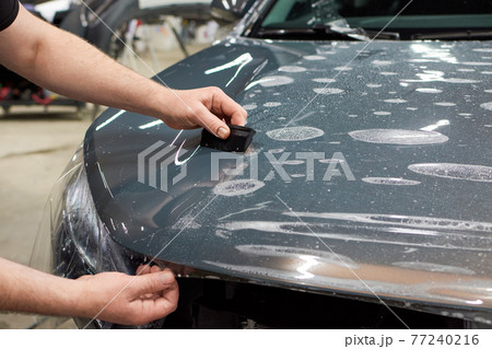 Installation of a protective paint and varnish transparent film on the car. PPF polyurethane film to protect the car paint from stones and scratches. 77240216