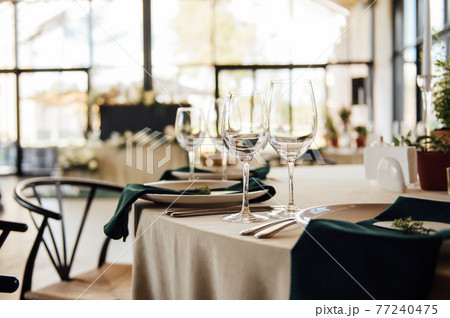 Luxurious restaurant. Luxurious interior, white tables, serving dishes and glasses for guests Luxurious restaurant. Luxurious interior, white tables, serving dishes and glasses for guests 77240475