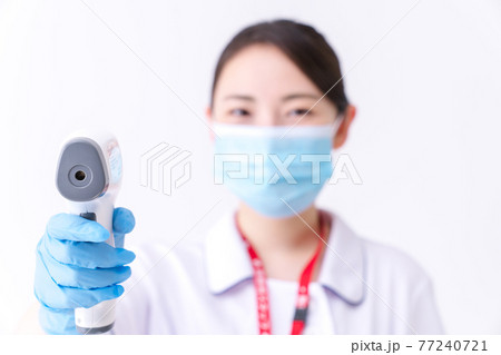 非接触体温計で体温測定をする看護師 非接触体温計で体温測定をする看護師 77240721