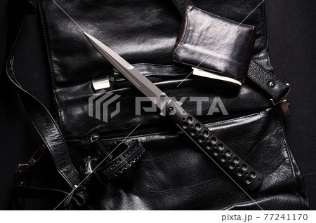 A large sharp knife and a purse of money. Knife on a leather briefcase. Clock and lantern. Black items on black. A large sharp knife and a purse of money. Knife on a leather briefcase. Clock and lantern. Black items on black. 77241170