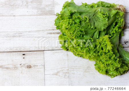Green lettuce leaves on brown wooden overlaid background with empty space for text, template design concept, food advertising, healthy food, spring and summer vitamins, food preparation ingredients 77246664