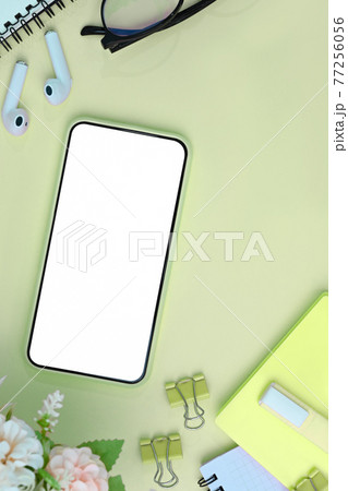 Mock up smart phone with blank screen, earphone, flowers and notebook on green background. 77256056