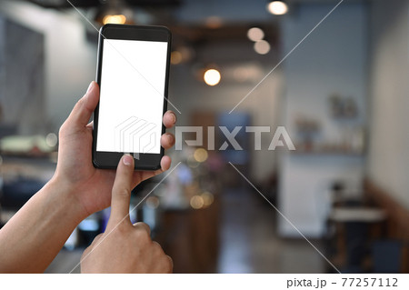 Man holding smartphone with modern coffee shop blurred background. Blank screen for graphics display montage. Man holding smartphone with modern coffee shop blurred background. Blank screen for graphics display montage. 77257112