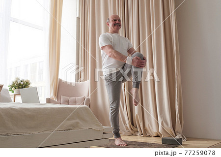 Senior handsome sportman doing stretching and balancing yoga exercise at home Senior handsome sportman doing stretching and balancing yoga exercise at home 77259078