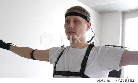 athletic man with beard wears motion capture suit with sensors headset moving in virtual reality taking something and looking at his hands excited experience cyber space online 77259382