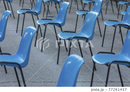Rows and columns of nondescript blue plastic chairs, consecutive, arranged in a line, at similar intervals of space, facing the same place. Retiro Park, Madrid, Spain. Rows and columns of nondescript blue plastic chairs, consecutive, arranged in a line, at similar intervals of space, facing the same place. Retiro Park, Madrid, Spain. 77261437