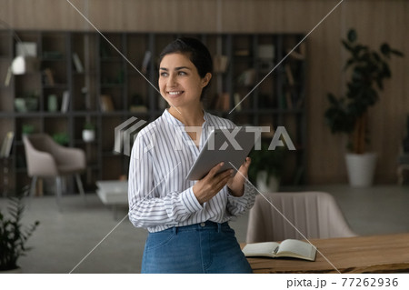 Dreamy smiling Indian businesswoman holding tablet, looking to aside Dreamy smiling Indian businesswoman holding tablet, looking to aside 77262936