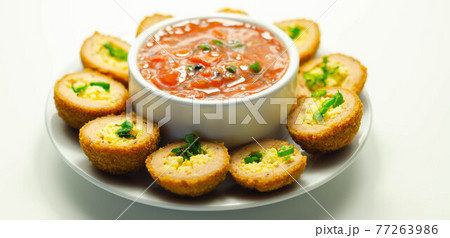 Mini scotch eggs with tomato sauce served on the white ceramic plate 77263986
