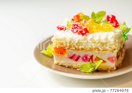 A portion of cream cake with pieces of colorful jelly and sprinkled with coconut flakes A portion of cream cake with pieces of colorful jelly and sprinkled with coconut flakes 77264076