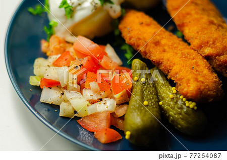 Breaded and herbed chicken breast fillet served with mashed potatoes,  tomato salad with onions and gherkin 77264087