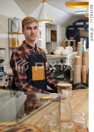 waiter in apron in coffee shop, barista is happy to work in the cafeteria 77264106