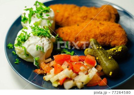 Breaded and herbed chicken breast fillet served with mashed potatoes, tomato salad with onions and gherkin Breaded and herbed chicken breast fillet served with mashed potatoes, tomato salad with onions and gherkin 77264580
