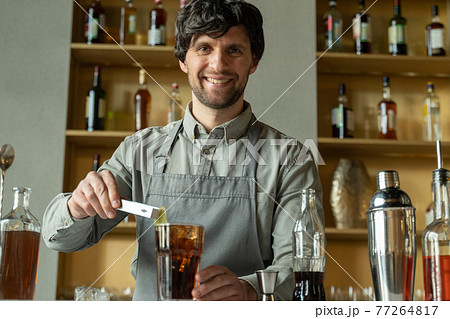 A professional bartender decorates the cocktail with lime. The bartender prepares a cocktail with whiskey and Cola. Preparing cocktails at the bar. 77264817