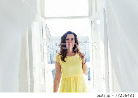 portrait of a beautiful brunette woman in a yellow summer dress by the window portrait of a beautiful brunette woman in a yellow summer dress by the window 77266431