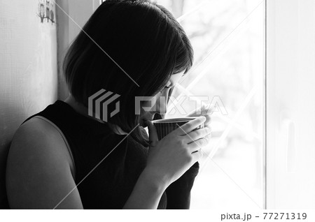 black and white portrait of a young brunette girl in black with a big cup of tea by the window 77271319