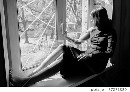 black and white portrait of a beautiful black-haired girl sitting on a windowsill in a long tight-fitting dark dress 77271320