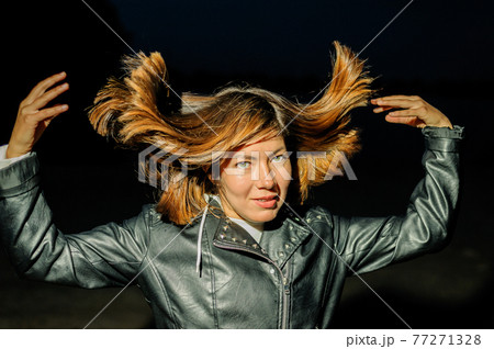 young woman in a black leather jacket throws up her hair 77271328