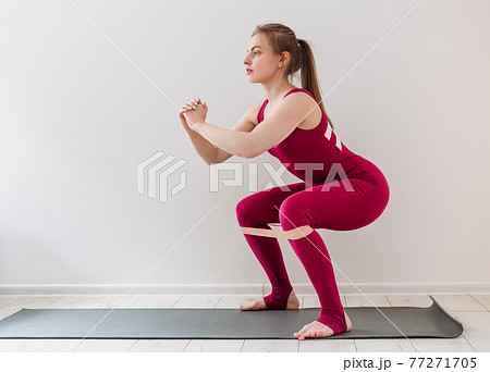 Athletic young woman makes side bar. Girl warms up legs, using fitness rubber band. Pink rubber for home exercises. Indoor and outdoor workout. Sport and healthy active lifestyle concept. Athletic young woman makes side bar. Girl warms up legs, using fitness rubber band. Pink rubber for home exercises. Indoor and outdoor workout. Sport and healthy active lifestyle concept. 77271705