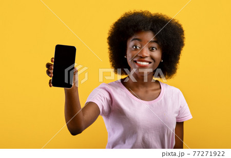 Positive african american woman showing cellphone with space for mobile app design on screen over yellow background 77271922