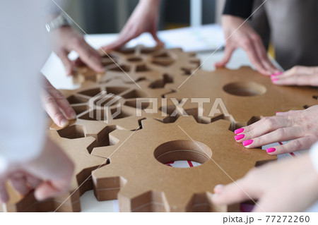 Employees connect together wooden gears on work table 77272260
