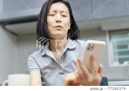 疲れた表情でスマートフォンを持つ女性 77283374