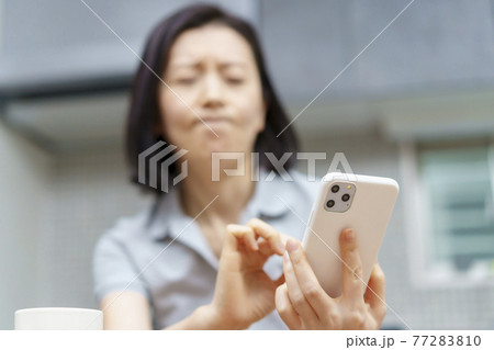 ストレスを抱えた表情でスマホを見る女性 ストレスを抱えた表情でスマホを見る女性 77283810