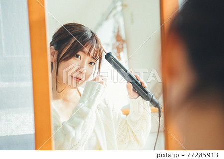 ヘアアイロンを使う若い女性 77285913