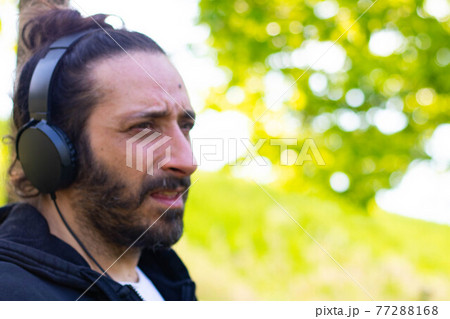 Hippy man with beard and headphones listening music outdoors on the garden 77288168