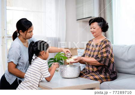 Asian child girl and her mother pouring water on hands of elder senior or respected grandparents for celebrate Songkran in new year water festival. Asian child girl and her mother pouring water on hands of elder senior or respected grandparents for celebrate Songkran in new year water festival. 77289710