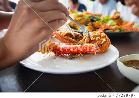 Woman hand holding fork dipping in piece of fried lobster shrimp with garlic on the plate in the restaurant. 77289797